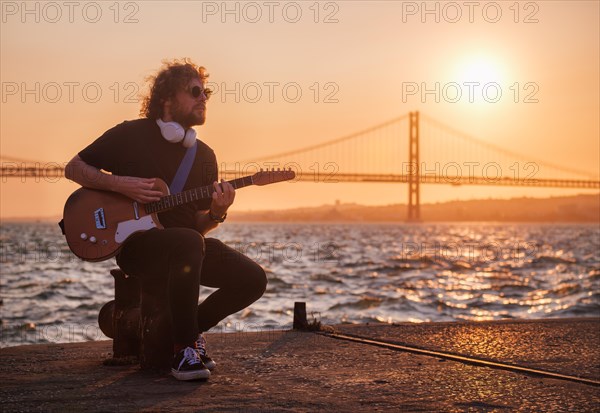 Hipster street musician in black playing electric guitar in the street on sunset