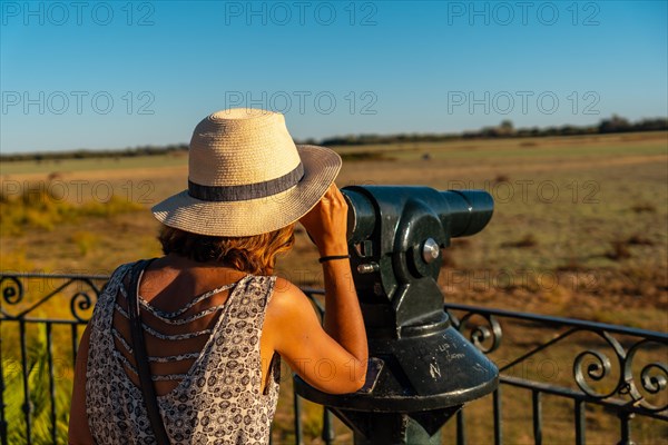 A young woman with binoculars looking at the horses grazing in the Donana park next to the El Rocio Sanctuary