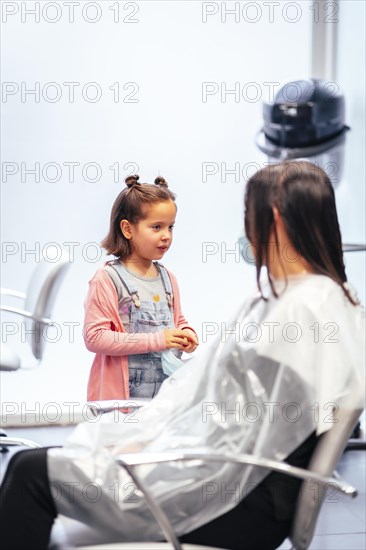 Client sitting waiting for the dye to dry and meanwhile talking to her daughter. Reopening with security measures for hairdressers in the Covid-19 pandemic