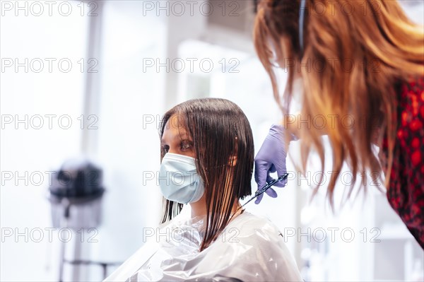 Hairdresser with mask and gloves cutting the ends of the hair to the client. Reopening with security measures for hairdressers in the Covid-19 pandemic