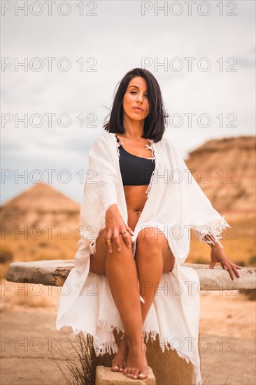 Lifestyle of a young brunette Caucasian girl in a white dress sitting in a beautiful desert