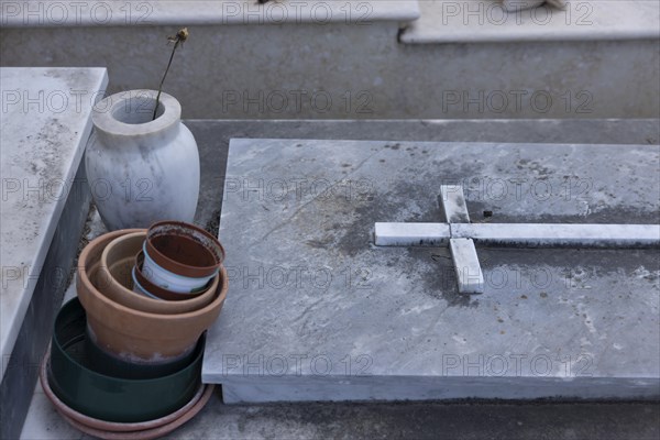 Grave with a single wilted flower in a vase and empty flower pots