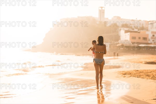A young mother with her six-month-old baby at sunset on a beach