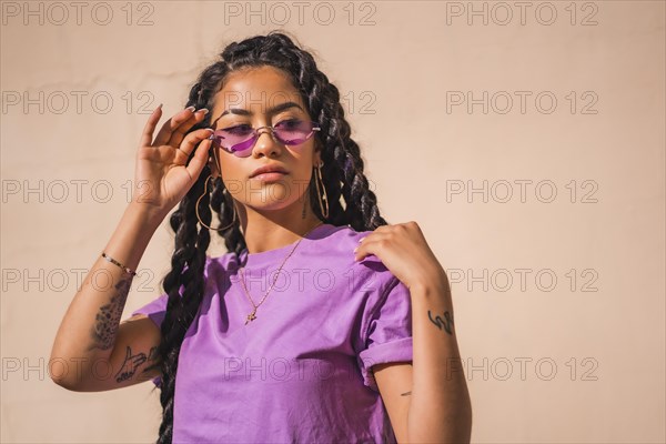 Urban session. Young dark-skinned woman with long braids wearing purple glasses on a plain background