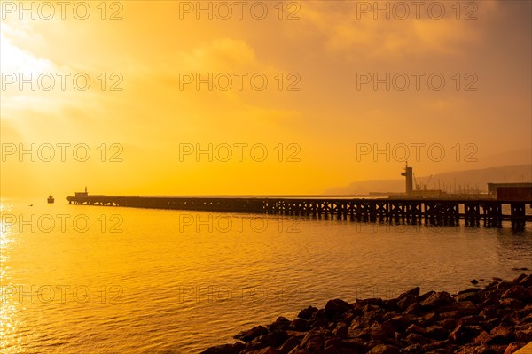 Old loading dock called Cable Frances at orange sunset on the beach of San Miguel in the city of Almeria