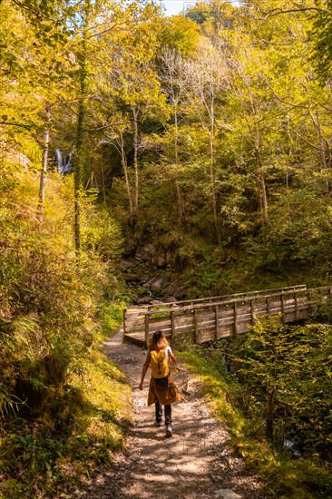 A young woman in autumn heading to Passerelle de Holtzarte in the forest or jungle of Irati