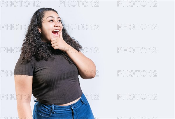 Happy young woman holding chin looking at an advertisement to side. Excited latin woman with hand on chin looking a promo to the side isolated