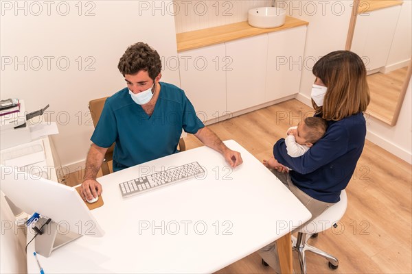 High angle view of a woman with baby in arms in a pediatric appointment sitting and talking with a doctor