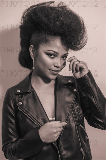 A vertical grayscale of a cute young smiling hipster female in a leather jacket posing at the camera