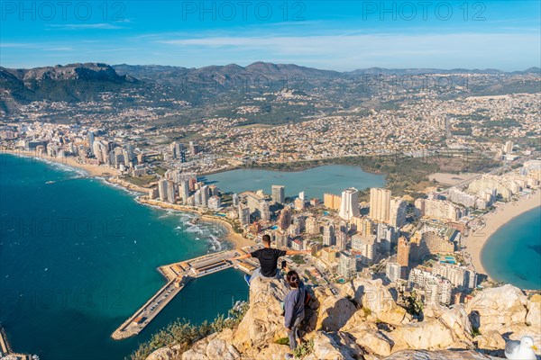 A young man sitting on top of the Penon de Ifach Natural Park with the city of Calpe in the background