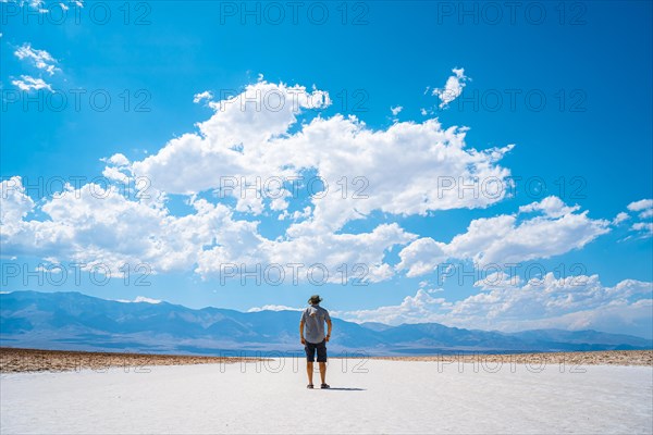 A young man jumping with a blue shirt on the white salt of Badwater Basin