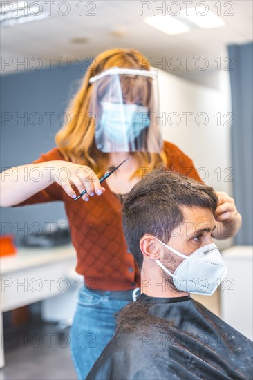 Hairdressers after the Coronavirus pandemic. Caucasian hairdresser with face mask and protective screen