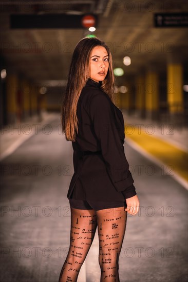 Young caucasian model with black jacket posing in an empty underground car park. Night urban session in the city