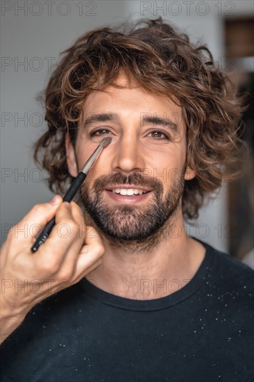 Street style with a young brunette caucasian man in a black suit and a white shirt in a luxurious hotel. In the pre-wedding makeup