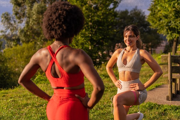 Caucasian blond girl and dark-skinned girl with afro hair doing stretching exercises in a park. Healthy life