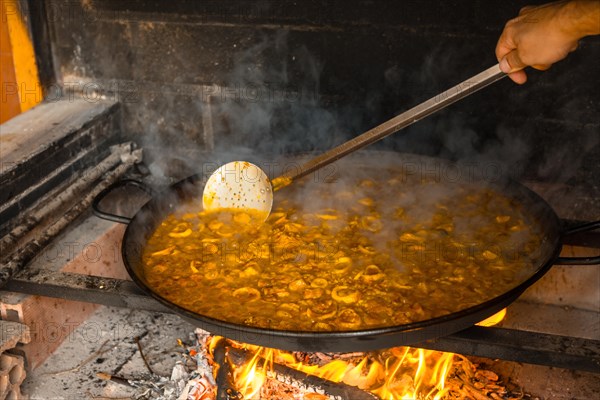 Stirring the rice from the Valencian paella with embers and vegetables. Traditional Spanish food