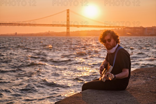 Hipster street musician in black playing electric guitar in the street on sunset