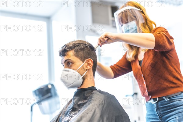 Hairdressers after the Coronavirus pandemic. Hairdresser with face mask and protective screen