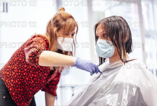 Hairdresser with mask and gloves cutting the ends with scissors to the client. Reopening with security measures for hairdressers in the Covid-19 pandemic