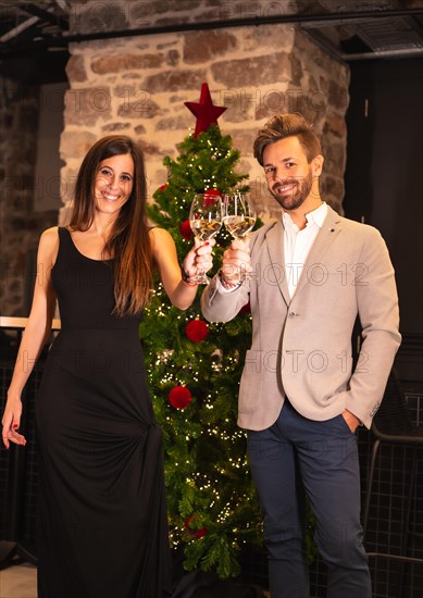 Romantic Christmas dinner for a young Caucasian couple. Toasting with the winged champagne glasses of the Christmas tree