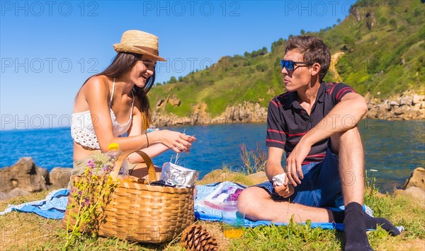 A young couple on a picnic drinking orange juice in the mountains by the sea enjoying the summer