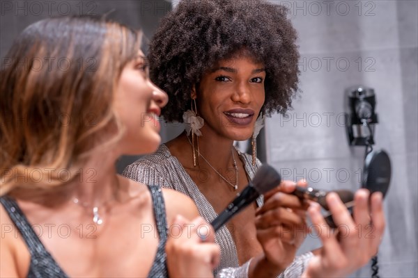 A young black girl with afro hair and a blonde Caucasian girl putting on makeup before the party with a smile. Exclusive party