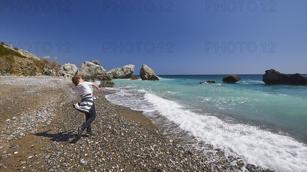 Boy hurls a stone in the air towards the sea