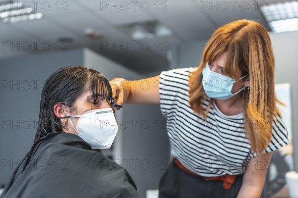 Hairdresser with face mask cutting bangs to the client. Safety measures for hairdressers in the Covid-19 pandemic. New normal