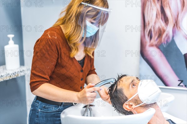 Reopening of hairdressing salons after the Coronavirus pandemic. Hairdresser with face mask and protective screen