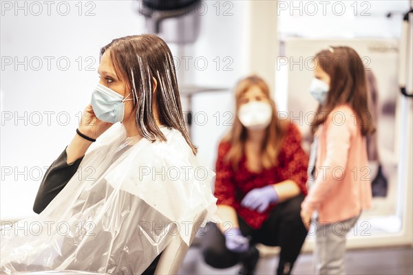Hairdresser with mask and gloves talking to the client's daughter while the client answers an important call. Reopening with security measures for hairdressers in the Covid-19 pandemic