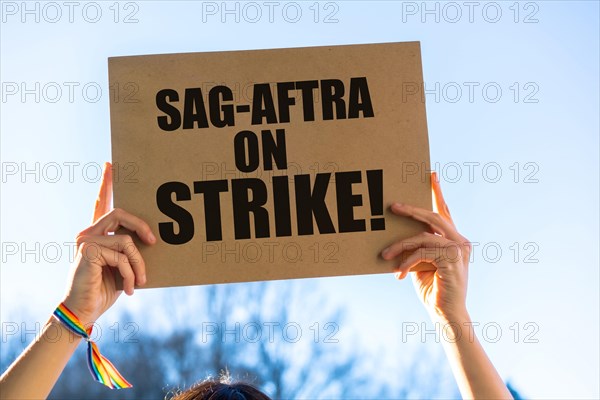 A female actress holding a sign with the slogan of the hollywood actors and writers strike with the blue sky in the background