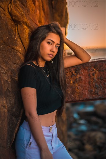 A young pretty brunette Latina with long straight hair in a short black T-shirt and pink pants. Portrait of the woman leaning on a sculpture with scab