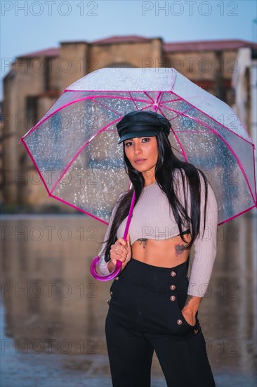 Posing of a young brunette Latina with a leather cap in the autumn rain with a transparent umbrella