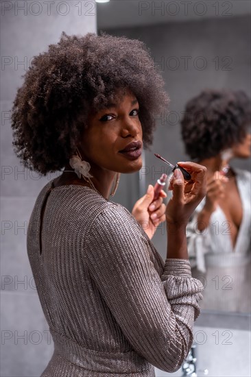 A young black girl with afro hair putting on makeup before the party with a smile. Exclusive party