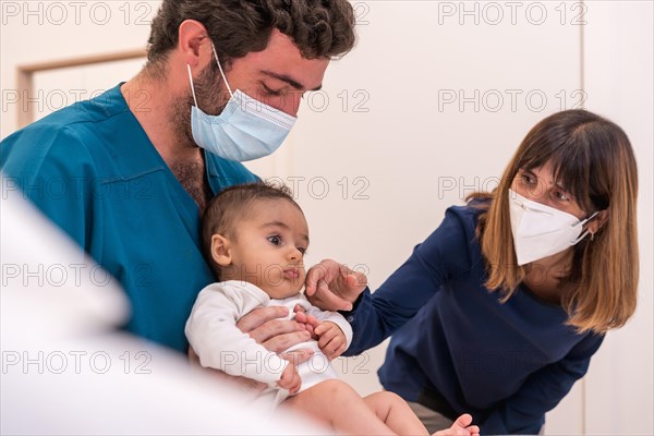 Doctor holding a baby next to his mother during a medical exam