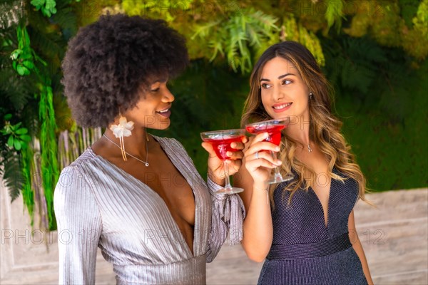 Two friends in gala dresses having a cocktail at a party in a hotel