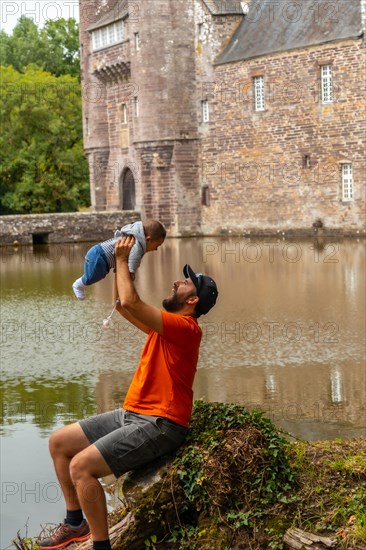 A young father with his baby visiting the medieval lakeside Chateau Trecesson