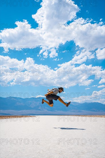 A young man jumping with a blue shirt on the white salt of Badwater Basin