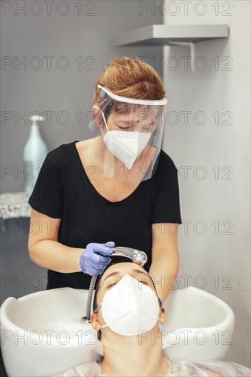 Hairdresser with mask and gloves washing the client's hair with water. Reopening with security measures of Hairdressers in the Covid-19 pandemic