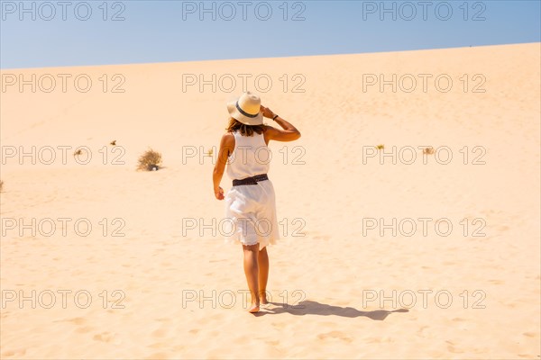 Tourist in white dress and hat walking through the dunes of the Corralejo Natural Park