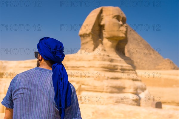 A young tourist enjoying and admiring the Great Sphinx of Giza dressed in blue and a blue turban. Cairo