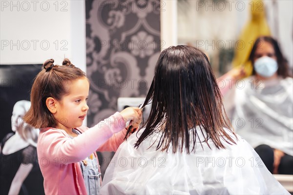 Client sitting by the mirror while waiting for her daughter to comb her hair. Reopening with security measures for hairdressers in the Covid-19 pandemic