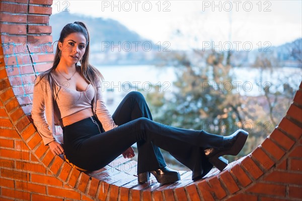 Portrait of a Caucasian brunette model sitting with the city in the background with a beautiful ponytail and a pink sweater. Street style fashion