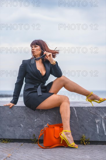 Fashion pose. Brunette girl sitting on the beach with a red bag and yellow shoes looking to the left