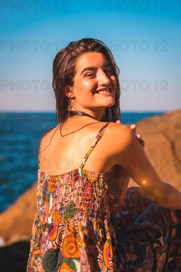 Portrait of a young Caucasian woman from behind smiling with wet hair and a floral dress by the sea