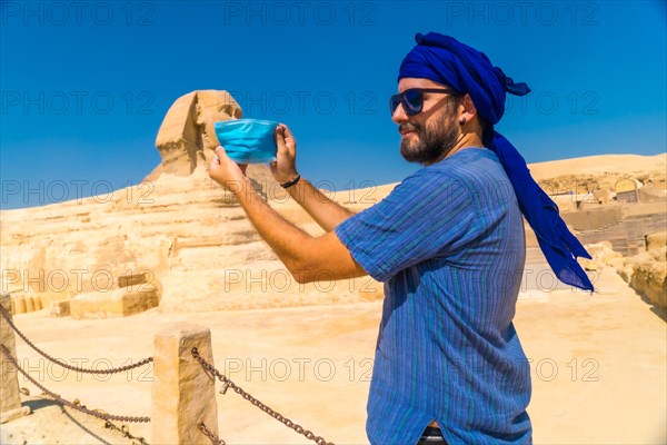 A young man putting on the mask facing the Great Sphinx of Giza and the Pyramids of Giza in the background