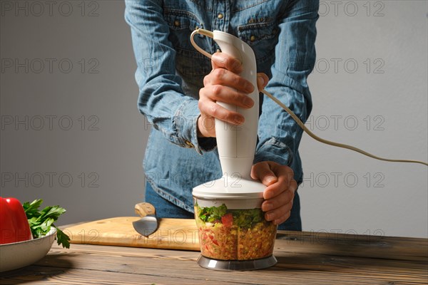 Hands of unrecognizable woman preparing salsa or guacamole in blender