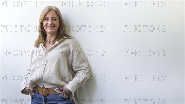 Beautiful caucasian mid aged woman looking at camera leaning on white wall. Copy space