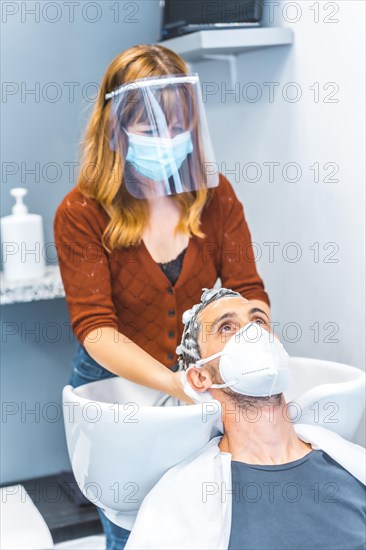 Hairdressers after the Coronavirus pandemic. Caucasian hairdresser with face mask and protective screen