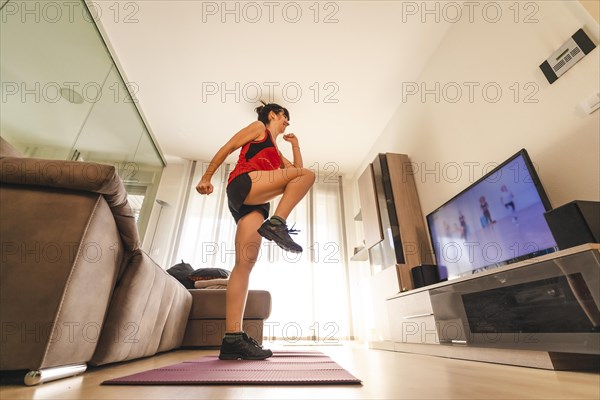 A young Caucasian woman doing exercises in the room following the instructions of the online teacher. Sport in the covid19 quarantine at home